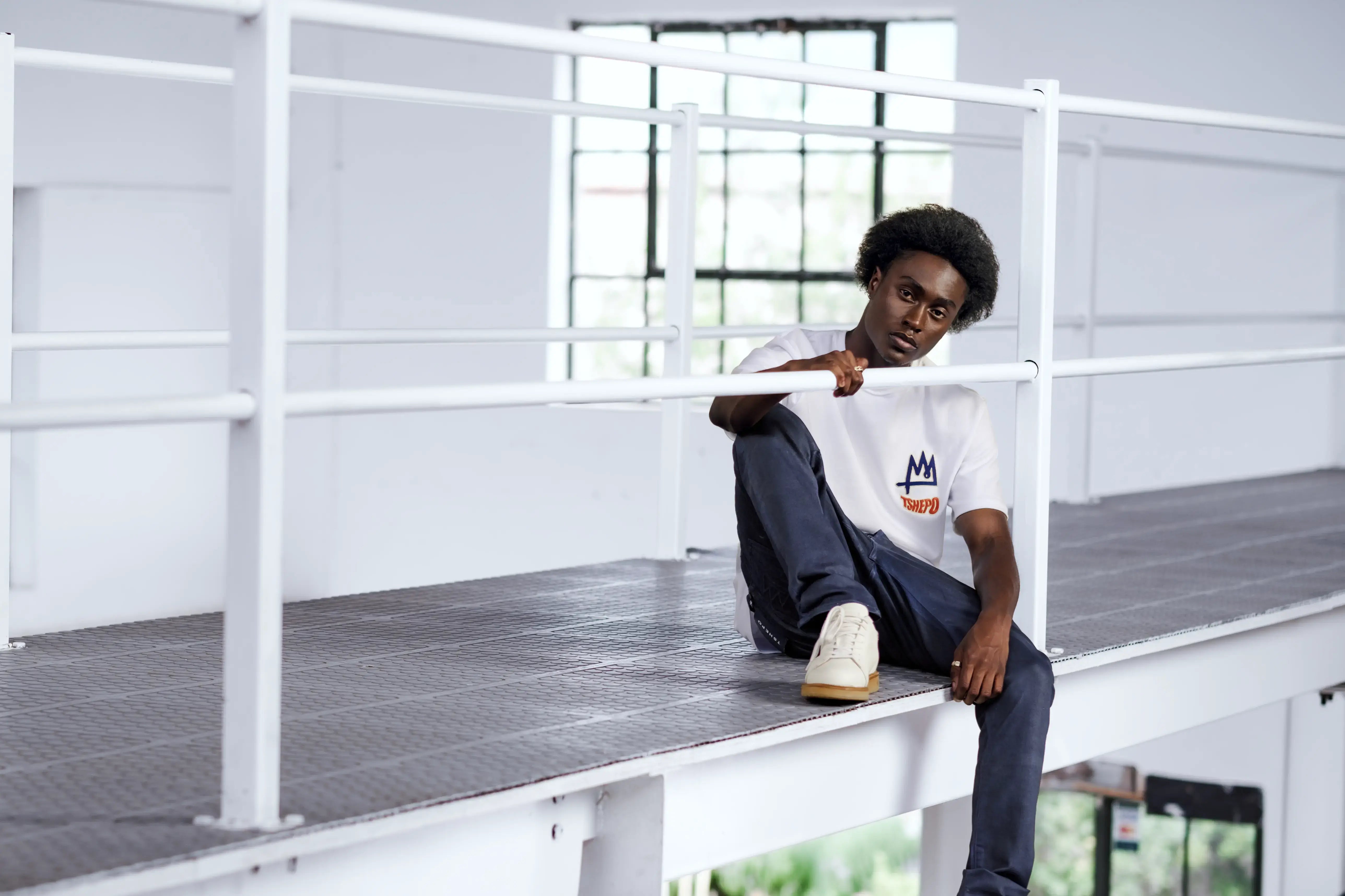 Tshepo Model sitting down in a warehouse setting wearing the white warp embroidered t-shirt